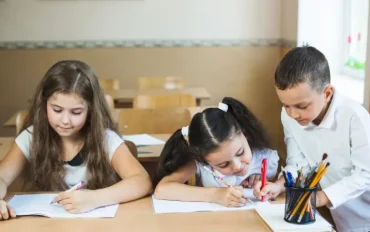 Three young students diligently working on writing assignments during an after school program in a bright classroom setting.