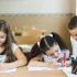 Three young students diligently working on writing assignments during an after school program in a bright classroom setting.