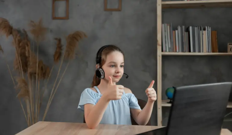 Young girl wearing headphones attending an online speech therapy session on a laptop