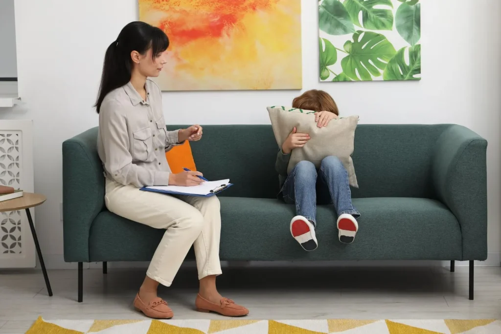 Child behaviour therapy session in Kerala with a therapist comforting and interacting with a shy child during counseling at a child development center.