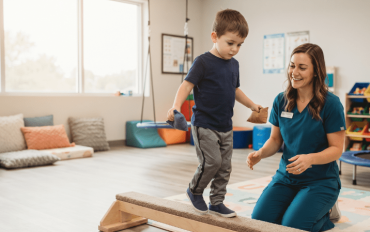 Young boy balancing with beanbags on a wooden beam while a pediatric occupational therapist watches during an ADHD and occupational therapy session.
